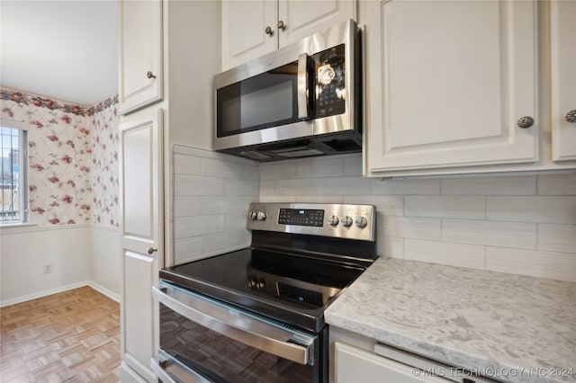 kitchen featuring light stone counters, light parquet floors, white cabinetry, and appliances with stainless steel finishes