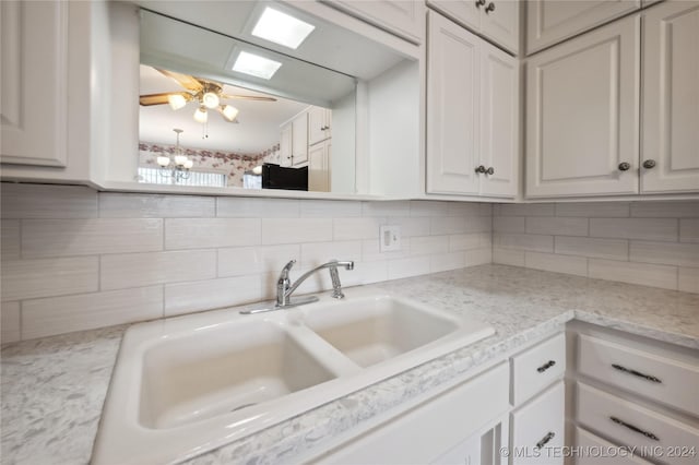 kitchen with decorative backsplash, a notable chandelier, sink, and white cabinetry