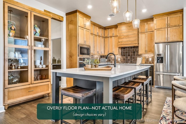 kitchen featuring dark hardwood / wood-style flooring, stainless steel appliances, a kitchen island with sink, decorative light fixtures, and a breakfast bar area