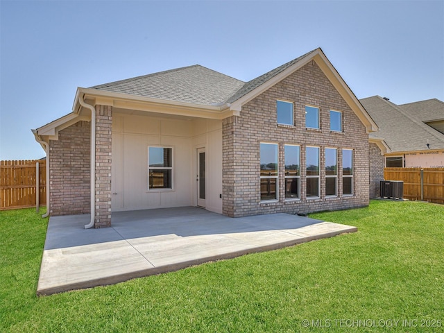 back of property with central AC unit, fence private yard, a lawn, a shingled roof, and a patio