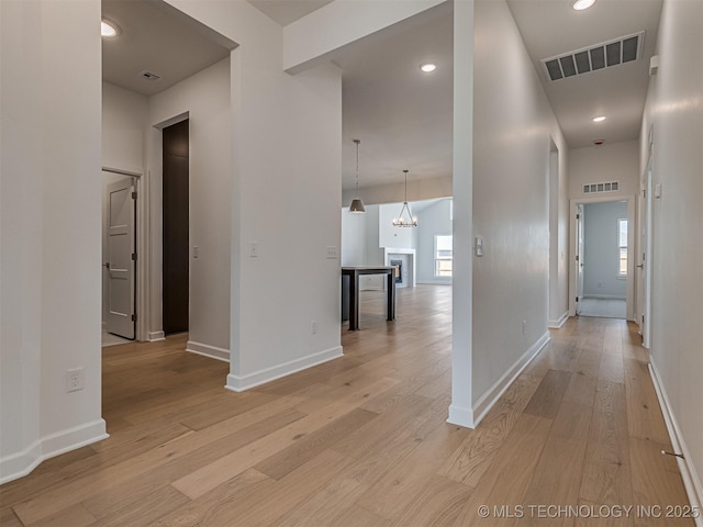 hall featuring light wood-type flooring, baseboards, visible vents, and a notable chandelier