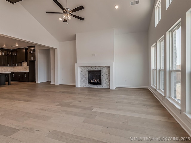 unfurnished living room featuring a wealth of natural light, a ceiling fan, visible vents, and high vaulted ceiling