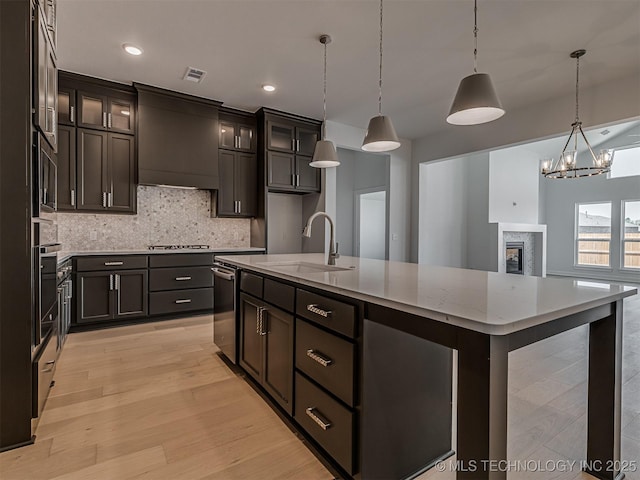 kitchen featuring a sink, custom exhaust hood, decorative backsplash, light stone counters, and appliances with stainless steel finishes