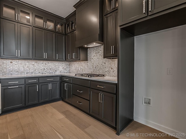 kitchen featuring stainless steel gas cooktop, tasteful backsplash, light wood-style floors, light countertops, and premium range hood