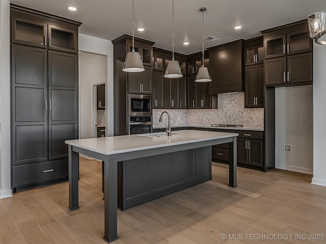 kitchen featuring light wood finished floors, stainless steel appliances, a sink, decorative backsplash, and custom range hood