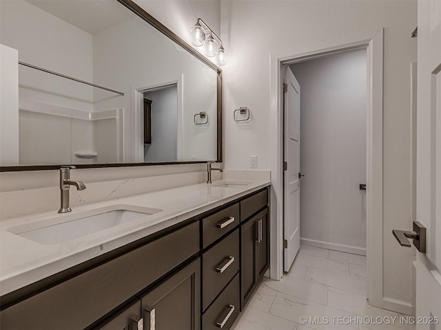 bathroom featuring marble finish floor, baseboards, a sink, and double vanity