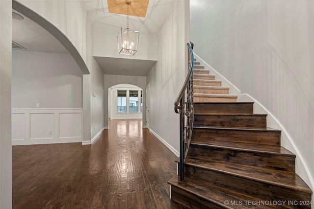 foyer entrance with dark wood-type flooring, a towering ceiling, and a chandelier