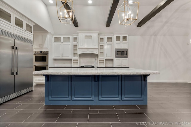 kitchen featuring an inviting chandelier, built in appliances, pendant lighting, a center island with sink, and white cabinets