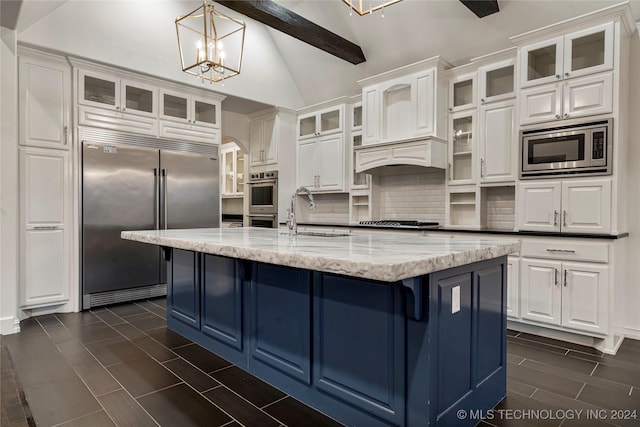 kitchen with white cabinetry, sink, light stone countertops, built in appliances, and an island with sink