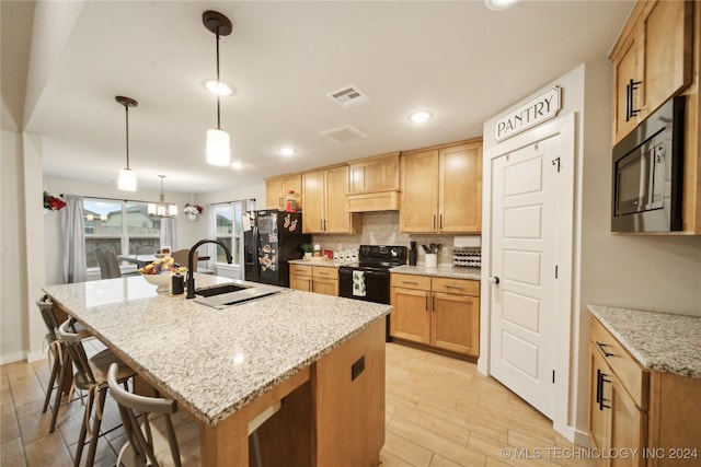 kitchen with light stone countertops, tasteful backsplash, pendant lighting, a center island with sink, and black appliances