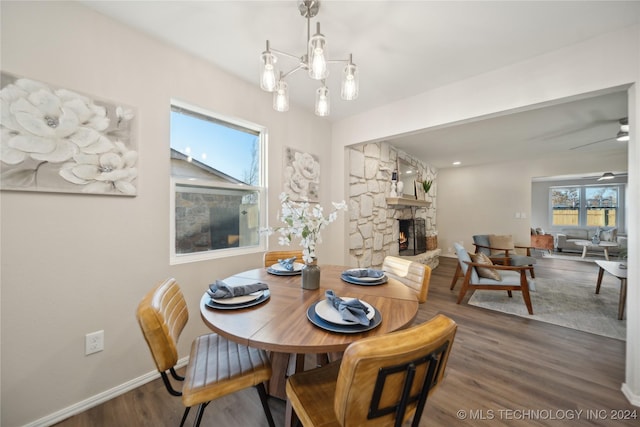 dining room featuring dark hardwood / wood-style flooring, a stone fireplace, and ceiling fan with notable chandelier