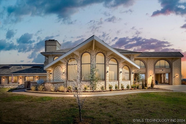 back house at dusk featuring a lawn