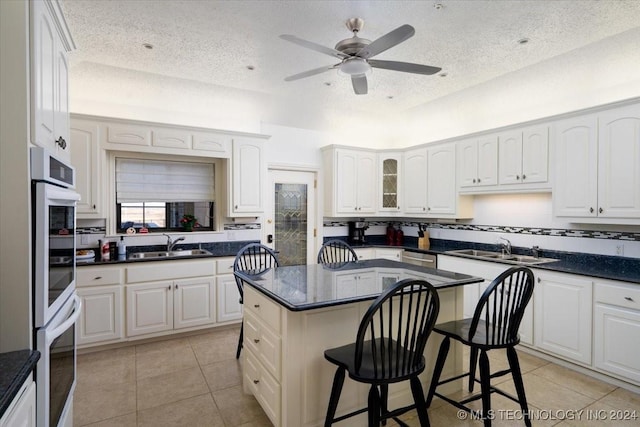 kitchen featuring a center island, white cabinets, a kitchen breakfast bar, ceiling fan, and a textured ceiling