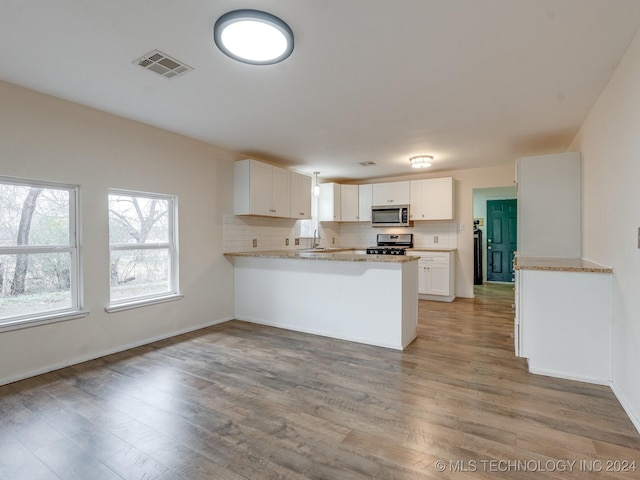 kitchen featuring tasteful backsplash, kitchen peninsula, light hardwood / wood-style floors, white cabinets, and appliances with stainless steel finishes