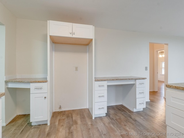 kitchen with built in desk, light hardwood / wood-style floors, white cabinetry, and light stone counters