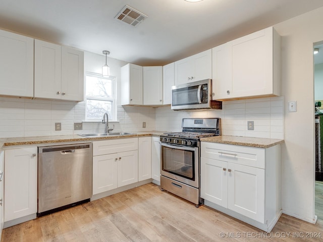 kitchen with appliances with stainless steel finishes, sink, decorative light fixtures, white cabinets, and light hardwood / wood-style floors