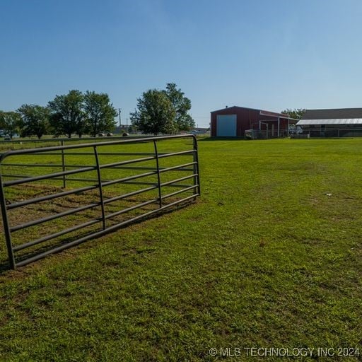 view of gate with a lawn, a rural view, and an outbuilding