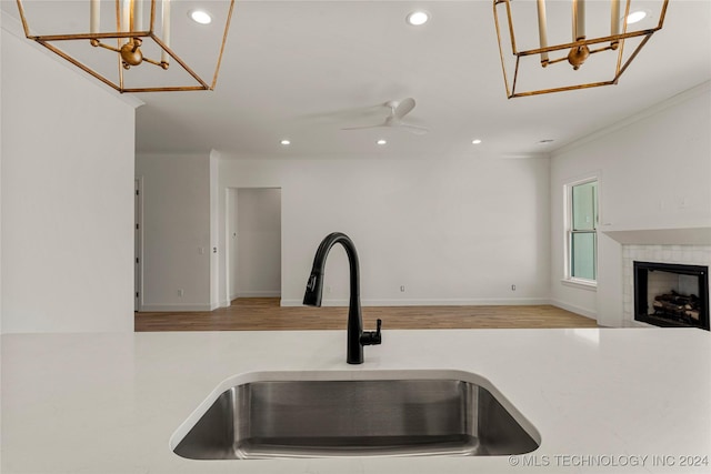 kitchen featuring sink, ceiling fan, light wood-type flooring, ornamental molding, and a tiled fireplace