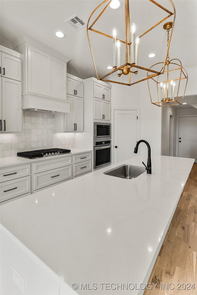 kitchen with light wood-type flooring, stainless steel appliances, sink, white cabinets, and hanging light fixtures