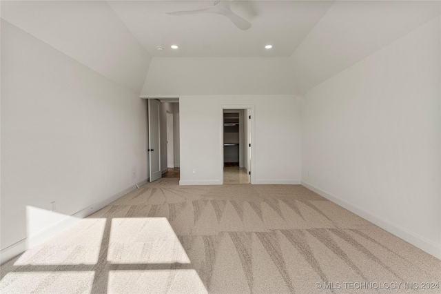 unfurnished bedroom with a walk in closet, light colored carpet, ceiling fan, a closet, and lofted ceiling