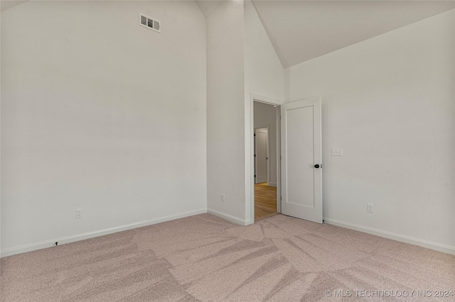 carpeted spare room with high vaulted ceiling