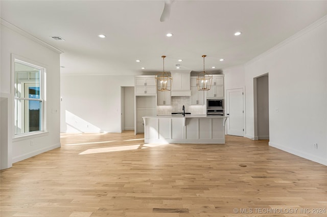 kitchen featuring sink, backsplash, pendant lighting, a center island with sink, and light wood-type flooring