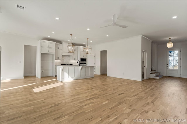 unfurnished living room featuring light hardwood / wood-style floors, ceiling fan, ornamental molding, and sink