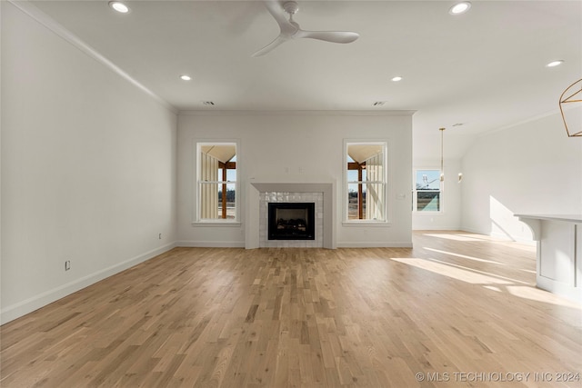 unfurnished living room with a tiled fireplace, crown molding, light hardwood / wood-style flooring, and ceiling fan with notable chandelier