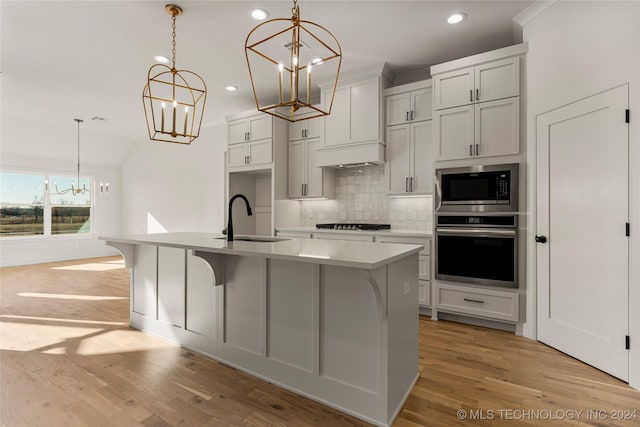 kitchen featuring sink, stainless steel appliances, backsplash, decorative light fixtures, and a kitchen island with sink