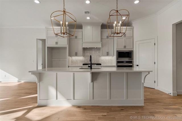 kitchen featuring oven, an island with sink, decorative light fixtures, and built in microwave