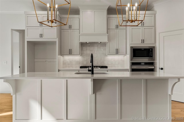 kitchen with pendant lighting, stainless steel appliances, a kitchen island with sink, and a notable chandelier