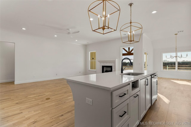 kitchen with a kitchen island with sink, ceiling fan with notable chandelier, sink, decorative light fixtures, and light hardwood / wood-style floors