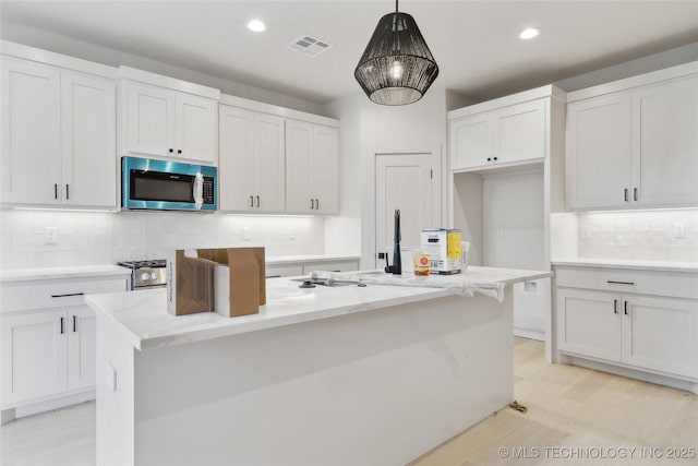 kitchen with decorative light fixtures, white cabinets, and an island with sink