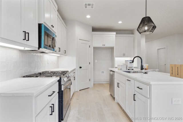 kitchen featuring decorative light fixtures, white cabinetry, appliances with stainless steel finishes, and a kitchen island with sink