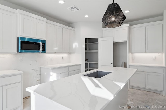 kitchen featuring hanging light fixtures, light stone countertops, white cabinetry, and a kitchen island