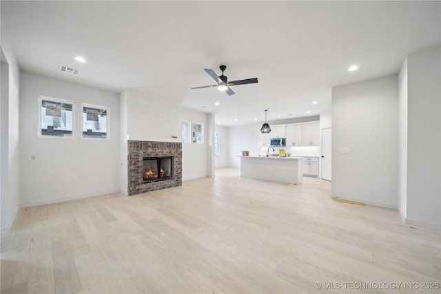 unfurnished living room with a brick fireplace, light hardwood / wood-style flooring, ceiling fan, and a healthy amount of sunlight