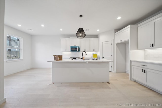 kitchen featuring decorative light fixtures, white cabinetry, and a kitchen island with sink