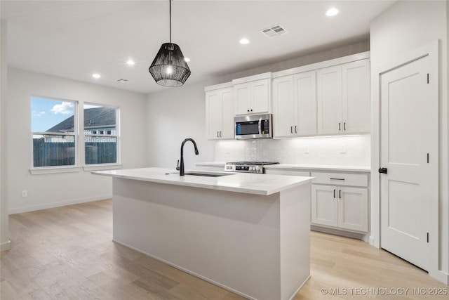 kitchen featuring hanging light fixtures, sink, a center island with sink, and white cabinets