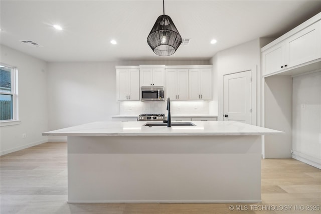 kitchen featuring decorative light fixtures, white cabinetry, sink, a kitchen island with sink, and light stone counters