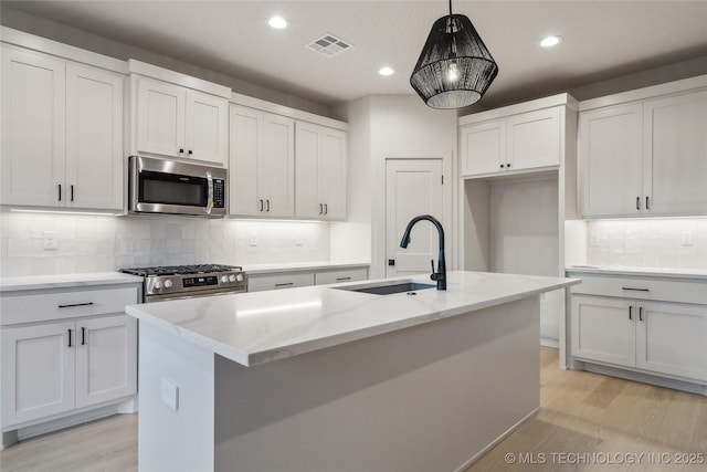 kitchen with sink, white cabinetry, stainless steel appliances, a center island with sink, and decorative light fixtures