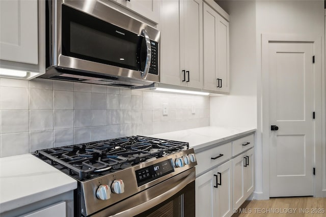 kitchen with white cabinetry, appliances with stainless steel finishes, light stone countertops, and decorative backsplash