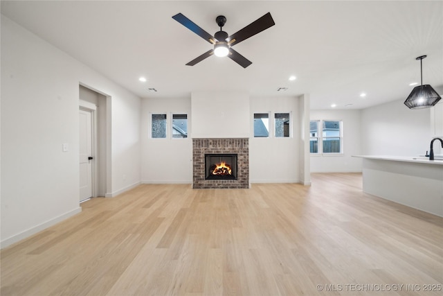 unfurnished living room with ceiling fan, sink, a fireplace, and light hardwood / wood-style floors