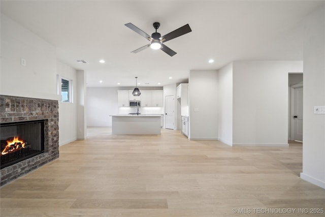 unfurnished living room with a brick fireplace, light hardwood / wood-style floors, and ceiling fan