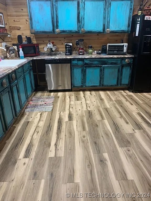 kitchen with sink, wooden walls, stainless steel dishwasher, light wood-type flooring, and black fridge with ice dispenser