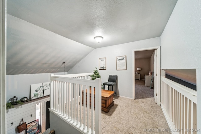 hallway with a textured ceiling, lofted ceiling, and light carpet