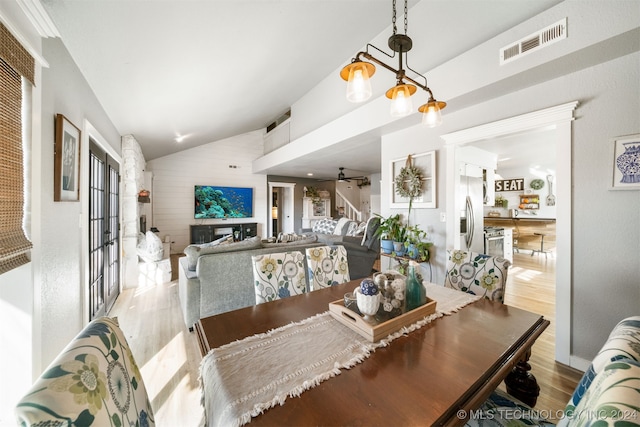 dining space with ceiling fan with notable chandelier, light hardwood / wood-style floors, and vaulted ceiling