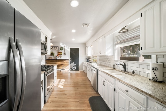 kitchen with white cabinets, sink, light hardwood / wood-style floors, light stone counters, and stainless steel appliances