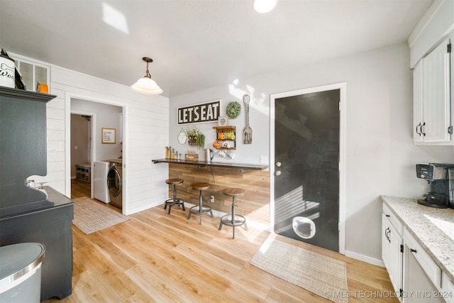 kitchen featuring pendant lighting, washer / dryer, white cabinetry, and light hardwood / wood-style flooring