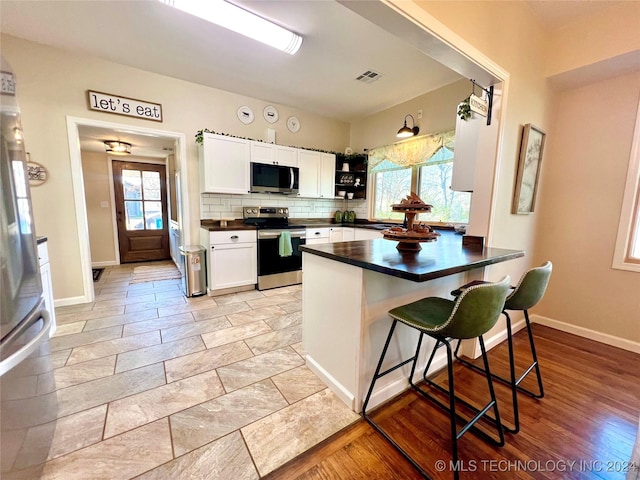 kitchen with white cabinetry, stainless steel appliances, kitchen peninsula, decorative backsplash, and a breakfast bar