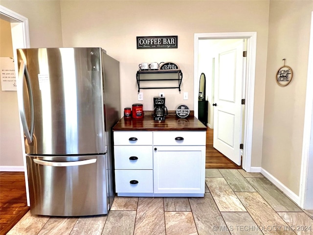 kitchen with white cabinets, butcher block countertops, and stainless steel refrigerator